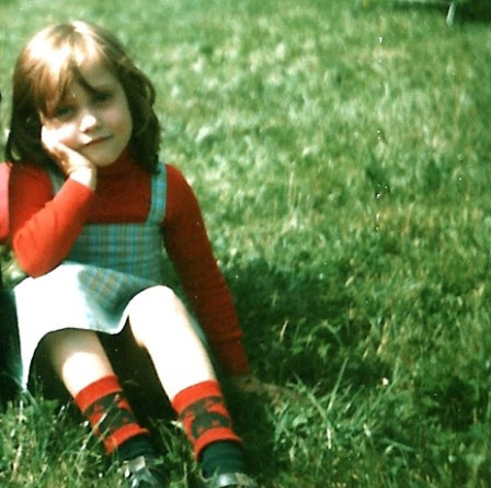 Moi à cinq ans, l'air boudeur, assise dans l'herbe